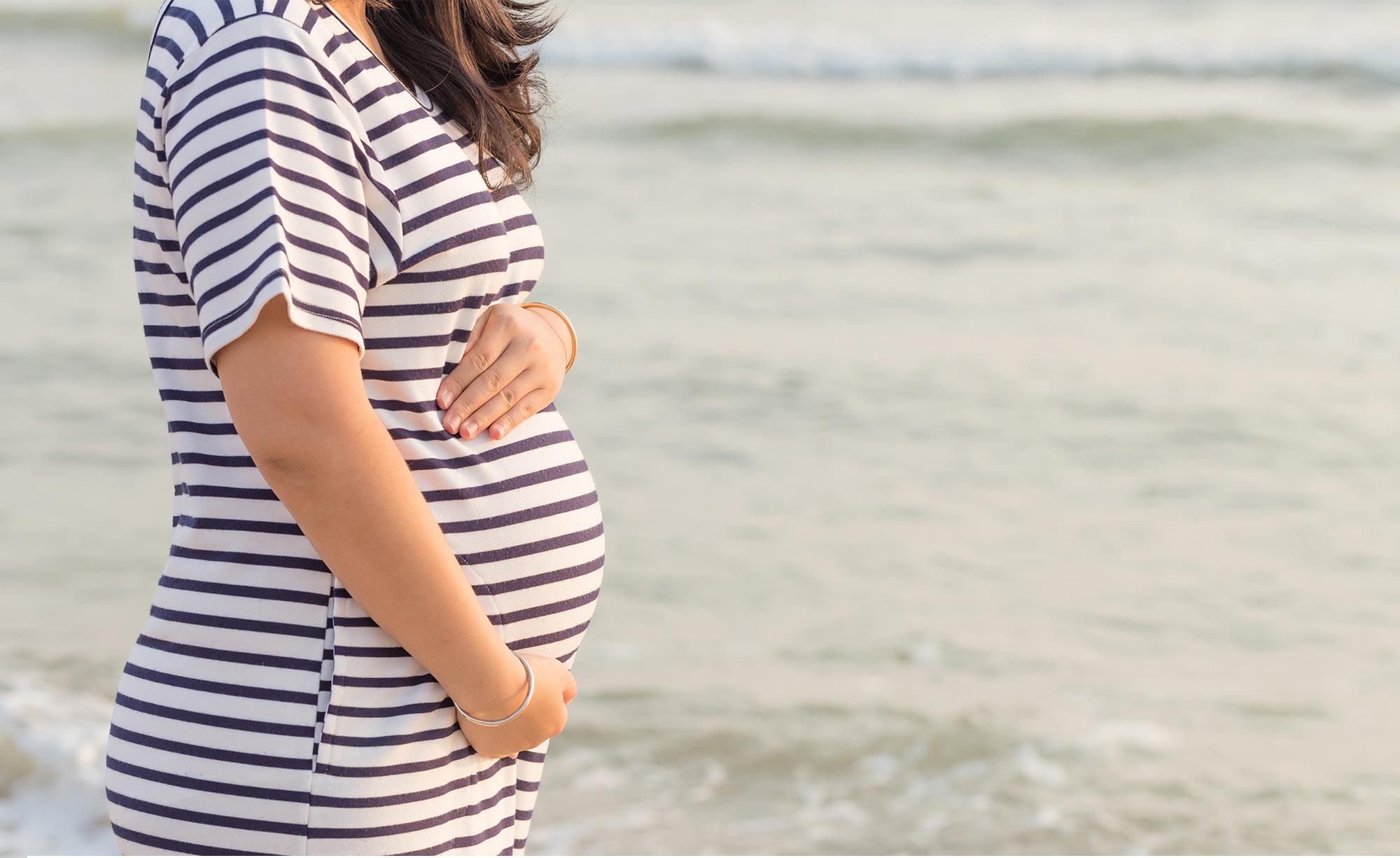 Pregnant woman holding belly in front of ocean
